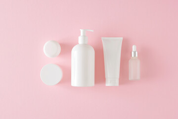 Skin care products concept. Flat lay composition made of white cosmetic bottles, cream jars and dropper bottle on pastel pink background. Blank label idea for branding mockup.