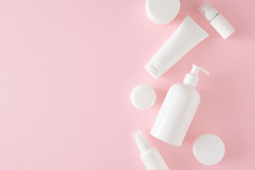 Skincare products concept. Flat lay photo of white pump bottle without label, cosmetic tubes and cream jars on pastel pink background with empty space. Blank label for branding mockup.