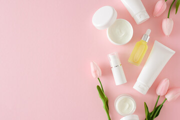 Obraz na płótnie Canvas Organic cosmetic concept. Top view photo of cosmetic tubes without label, cream jars, serum bottles and spring flowers on pastel pink background with empty space. Cosmetics mockup idea.