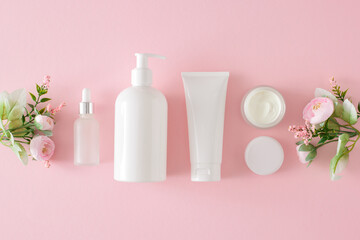 Organic beauty products concept. Top view photo of cosmetic tubes without label, serum bottles, cream jars and spring flowers on pastel pink background. Cosmetic mockup.