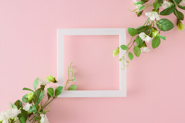 Spring holiday concept. Top view composition made of spring flowers and white frame in the middle on pastel pink background. Spring holiday card idea.