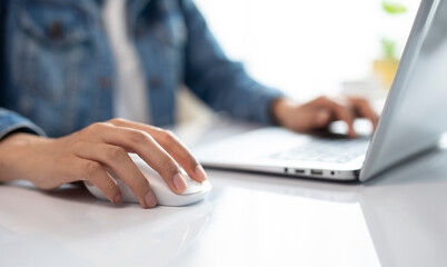 Casual young woman, freelance working on laptop computer and clicking wireless digital mouse in office table, close up
