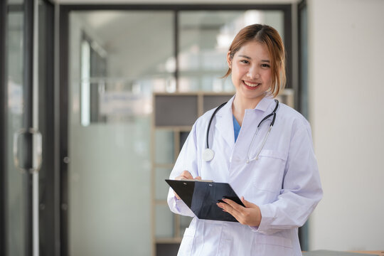Portrait of confident positive female doctor holding clipboard when standing at her office desk