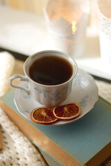 Vintage books, reading glasses, e-reader, cup of tea, bowl of biscuits and lit candle on the table. Selective focus.