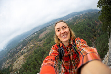 Naklejka premium female tourist taking a selfie portrait on top of a mountain - Happy smiling woman using her smartphone - Hiking and rock climbing.