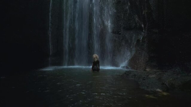 Beautiful blonde girl standing by the waterfall. Amazing waterfall Tukad on Bali