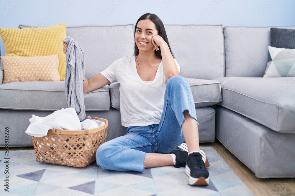 Poster young brunette woman doing laundry at home smiling with a happy and cool smile on face. showing teet