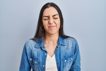 Hispanic woman standing over blue background with hand on stomach because indigestion, painful...