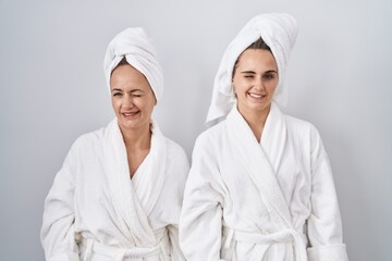 Middle age woman and daughter wearing white bathrobe and towel winking looking at the camera with sexy expression, cheerful and happy face.