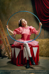 Beautiful little girl in festive pink dress posing with gymnastic hoop over dark vintage circus background. Concept of retro circus, holidays, dreams, art, fashion, vintage style © master1305