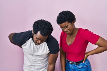 Young african american couple standing over pink background suffering of backache, touching back with hand, muscular pain