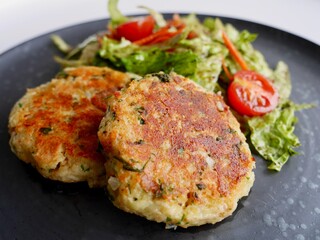 Traditional Austrian flat bread cheese dumplings, Kaspressknoedel, served with green salad on black ceramic plate.