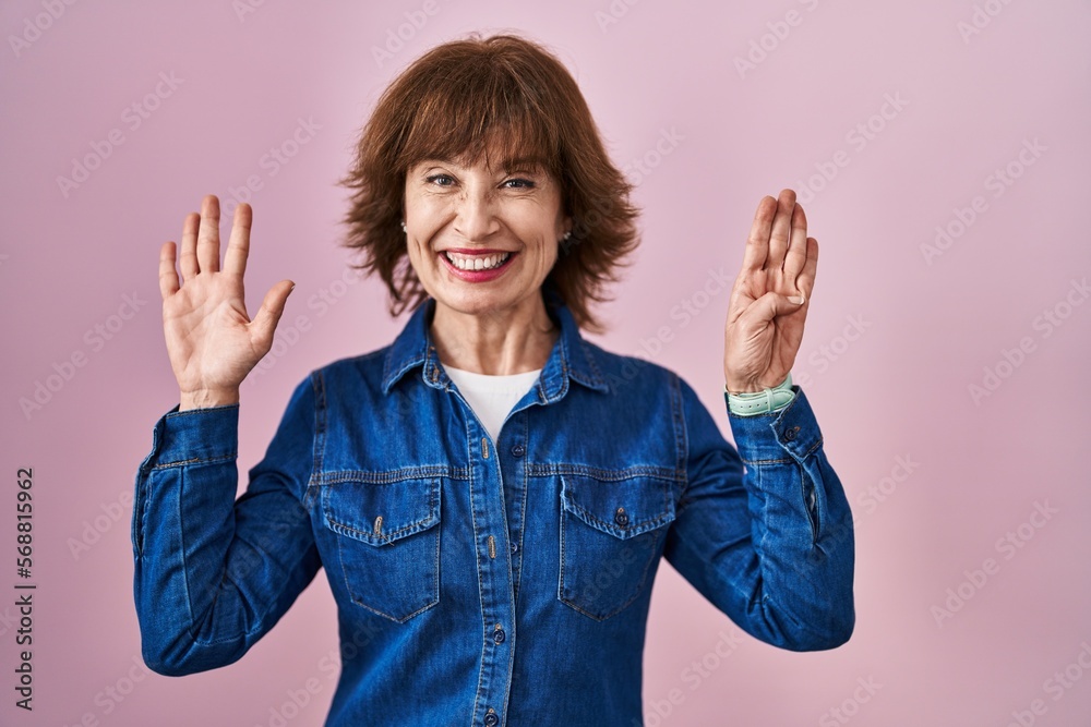 Wall mural Middle age woman standing over pink background showing and pointing up with fingers number nine while smiling confident and happy.