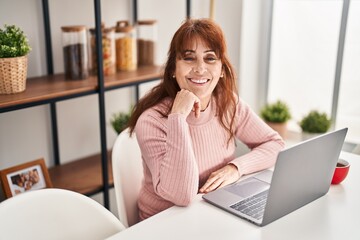 Middle age woman using laptop sitting on table at home