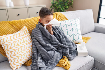 Adorable hispanic boy using napkin sitting on sofa at home