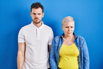 Young brazilian mother and son standing over blue background skeptic and nervous, frowning upset because of problem. negative person.