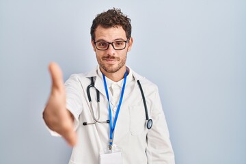 Fototapeta premium Young hispanic man wearing doctor uniform and stethoscope smiling friendly offering handshake as greeting and welcoming. successful business.