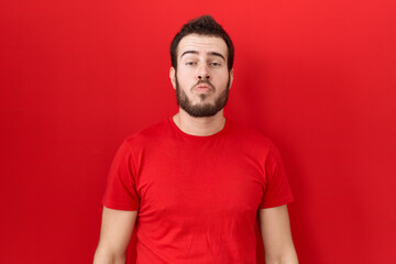 Young hispanic man wearing casual red t shirt looking at the camera blowing a kiss on air being lovely and sexy. love expression.