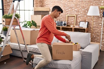 Young hispanic man unpacking cardboard box at new home