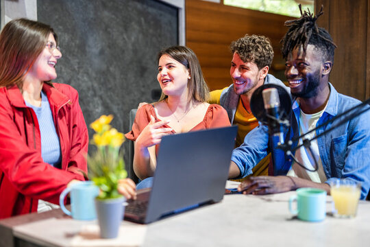 Four happy radio presenters having a good time on air, young people smiling happily while recording an audio broadcast at home studio, cheerful content creators co-hosting an internet podcast.