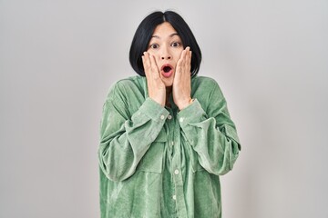 Young asian woman standing over white background afraid and shocked, surprise and amazed expression...