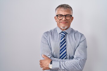 Hispanic business man with grey hair wearing glasses happy face smiling with crossed arms looking at the camera. positive person.