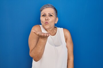 Middle age caucasian woman standing over blue background looking at the camera blowing a kiss with hand on air being lovely and sexy. love expression.