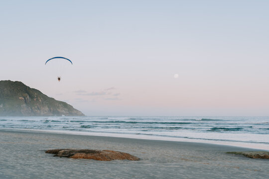 Paraglider mit Motor scwebt &uuml;ber dem Meer entlang am Praia do Luz zum Sonnenuntergang. Praia da Rosa