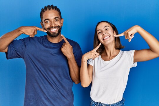 Young hispanic couple standing together smiling cheerful showing and pointing with fingers teeth and mouth. dental health concept.