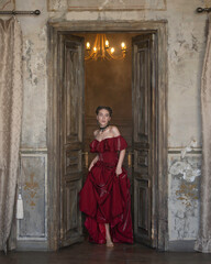 Fototapeta na wymiar A girl in a red dress enters a wooden door