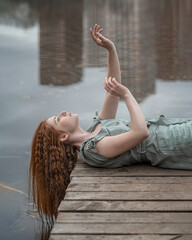 A girl with red hair lies on a wooden bridge with her hands up
