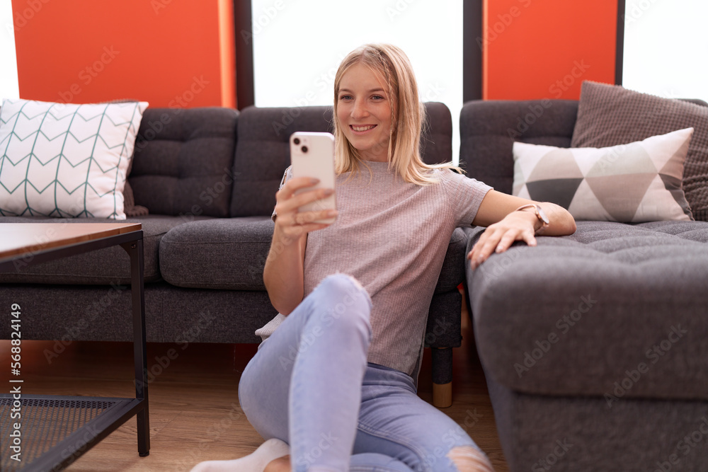 Canvas Prints Young blonde woman using smartphone sitting on floor at home