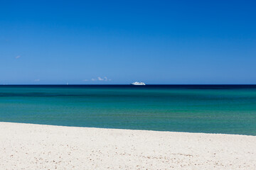 Clear turqoise water of Mediterranean sea with blue sky and vessel on horizon at Sardinia, Italy on sunny day. Amazing sea view.