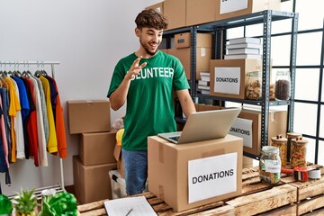 Young arab man wearing volunteer uniform having video call at charity center