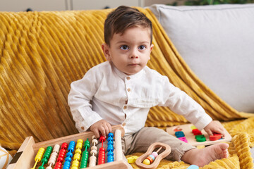 Adorable hispanic boy playing with abacus sitting on sofa at home