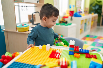 Adorable hispanic boy playing with play kitchen standing at kindergarten