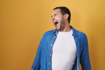 Hispanic man standing over yellow background angry and mad screaming frustrated and furious, shouting with anger. rage and aggressive concept.