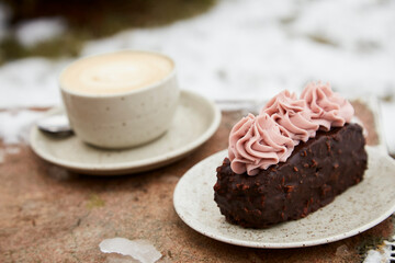 Aestetics vegan brownie witn no sugar cake dessert and cup of cappuccino outdoor at the snowy day. Coffee with dessert winter aesthetics