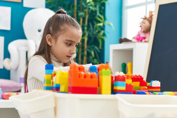 Obraz na płótnie Canvas Adorable hispanic girl playing with construction blocks sitting on table at kindergarten