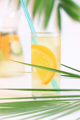 Lemonade and palm leaves. Drinking a cold drink through a straw. Lemonade with ice and an orange slice in a tall glass. Selective focus.