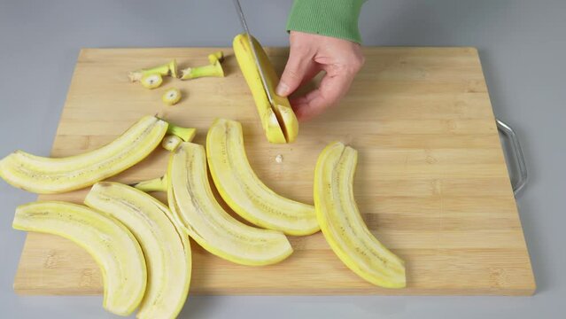 Slicing yellow bananas lengthwise with a knife on a kitchen board close-up. High quality 4k footage