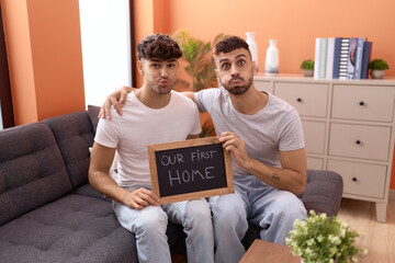 Homosexual gay couple holding blackboard with first home text puffing cheeks with funny face. mouth inflated with air, catching air.