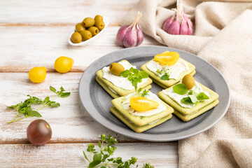 Green cracker sandwiches with cream cheese and cherry tomatoes on white wooden background. side view.