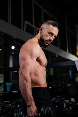 Fototapeta na wymiar A brutal muscular bearded man with abs holds a dumbbell in the gym. Active lifestyle, sports