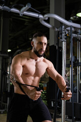 Fototapeta na wymiar A brutal muscular bearded man with a beautiful abs does cable machine exercises in the gym. Active lifestyle, sports