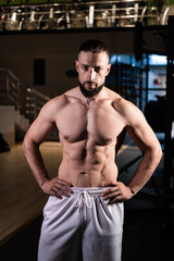 Obraz na płótnie Canvas A handsome bearded male athlete with a muscular body poses in the gym in white pants