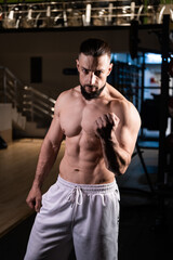 Fototapeta na wymiar A handsome bearded male athlete with a muscular body poses in the gym in white pants