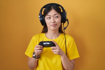 Chinese young woman playing video game holding controller smiling looking to the side and staring away thinking.