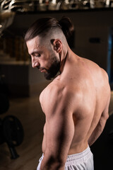 Fototapeta na wymiar A handsome bearded male athlete with a muscular body poses in the gym in white pants. Active lifestyle, sports
