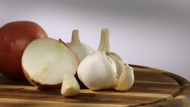 onions and garlic on a cutting board. a clove of garlic and half an onion lie with the whole. vegetables ready for cutting close-up. kitchen on a sunny day. High quality 4k footage